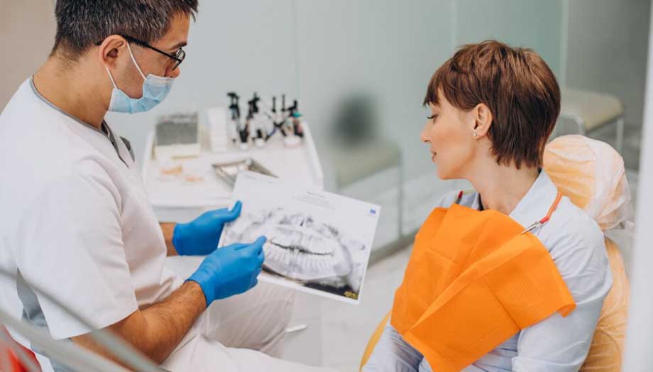 Imagen de un dentista mostrando placa de los dientes a una paciente mujer sentada en la silla del consultorio