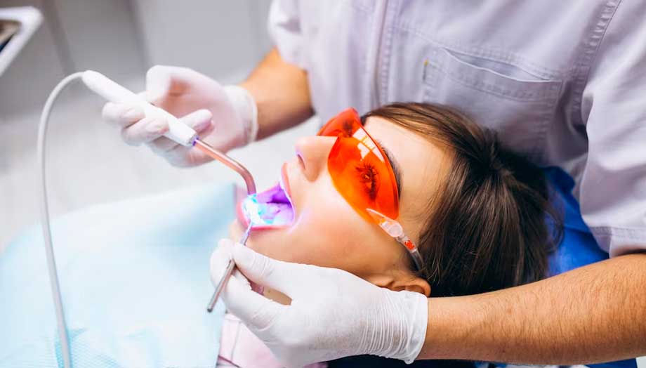 mujer con la boca abierta mientras un odontólogo la hace blanqueamiento dental con luz led