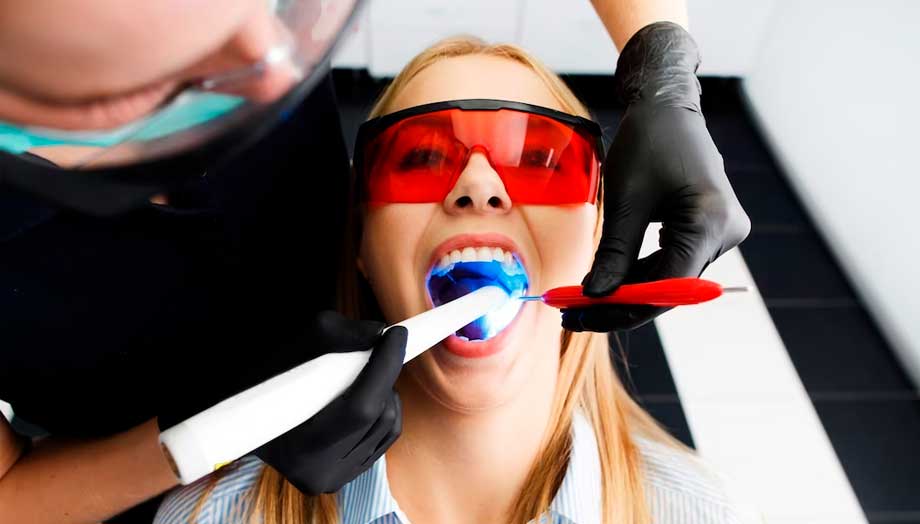 Imagen de una mujer con la boca abierta mientras endereza sus dientes rápido. El dentista trabaja en sus dientes con herramientas especializadas mientras ella está relajada en la silla del dentista.